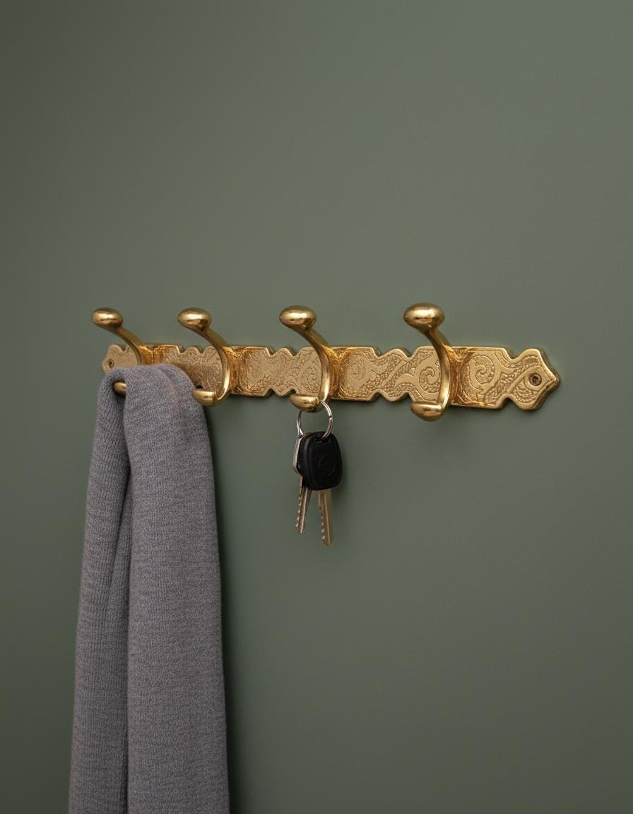 Gold decorative wall hook with keys and a gray garment against a green wall