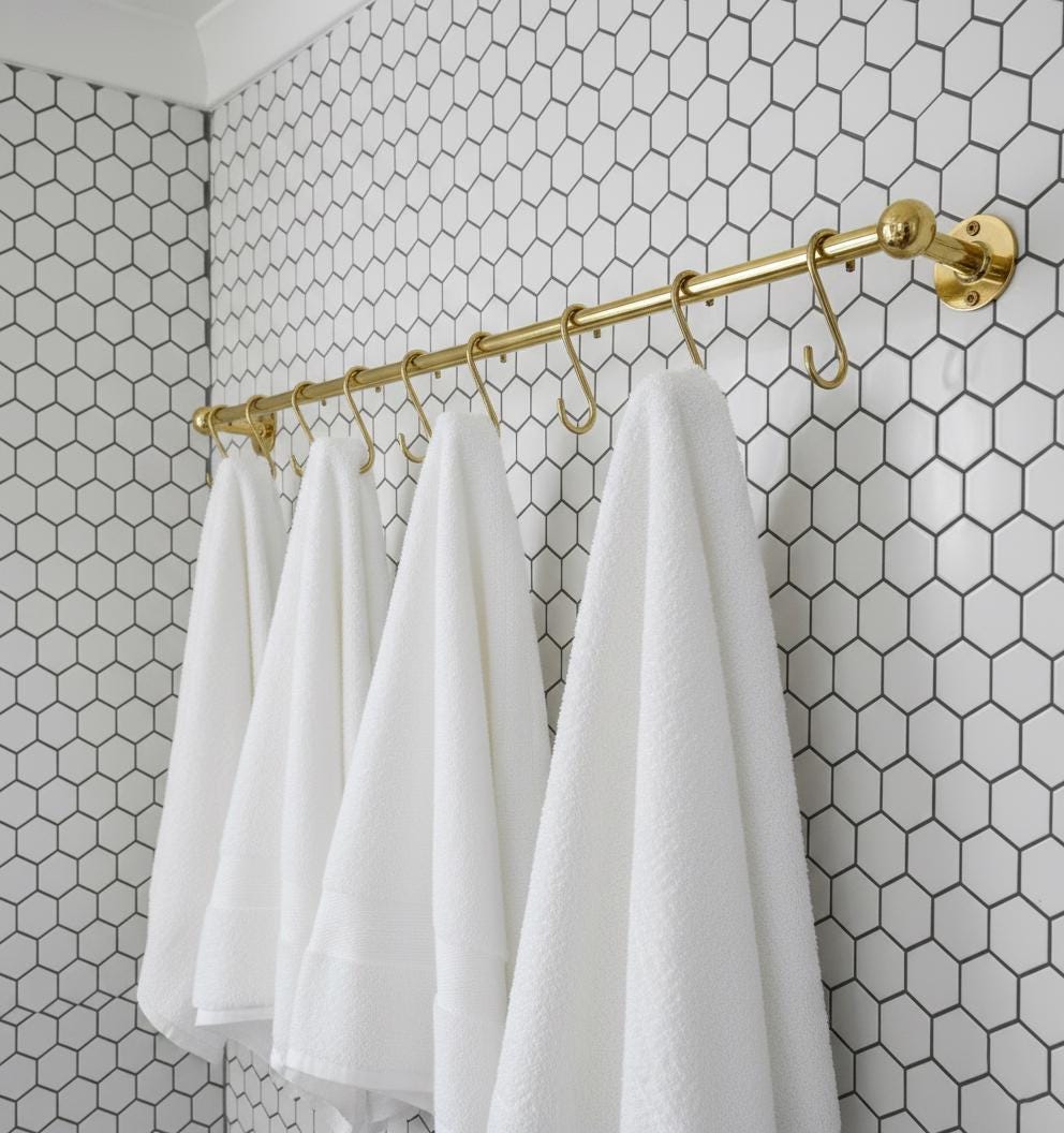 White towels hanging on a gold towel rack against a hexagonal tile wall.