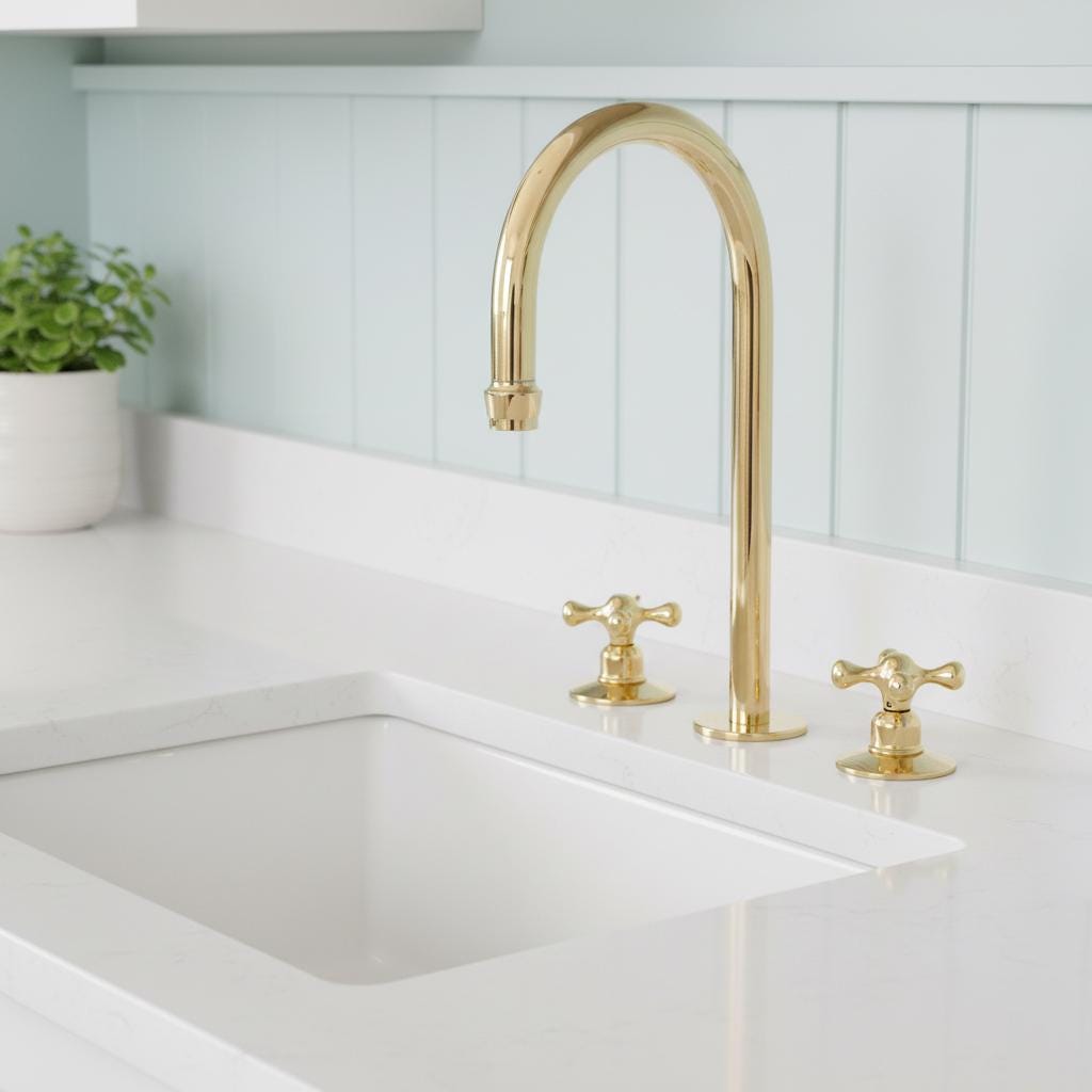 Gold kitchen faucet over a white sink with a light blue tiled wall in the background.