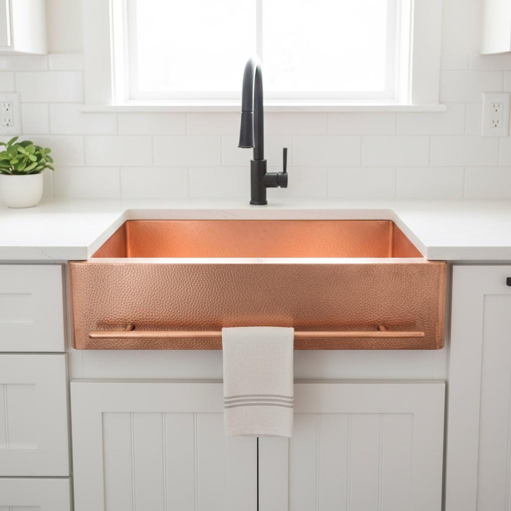 Copper farmhouse sink in a kitchen with white cabinets and black faucet.