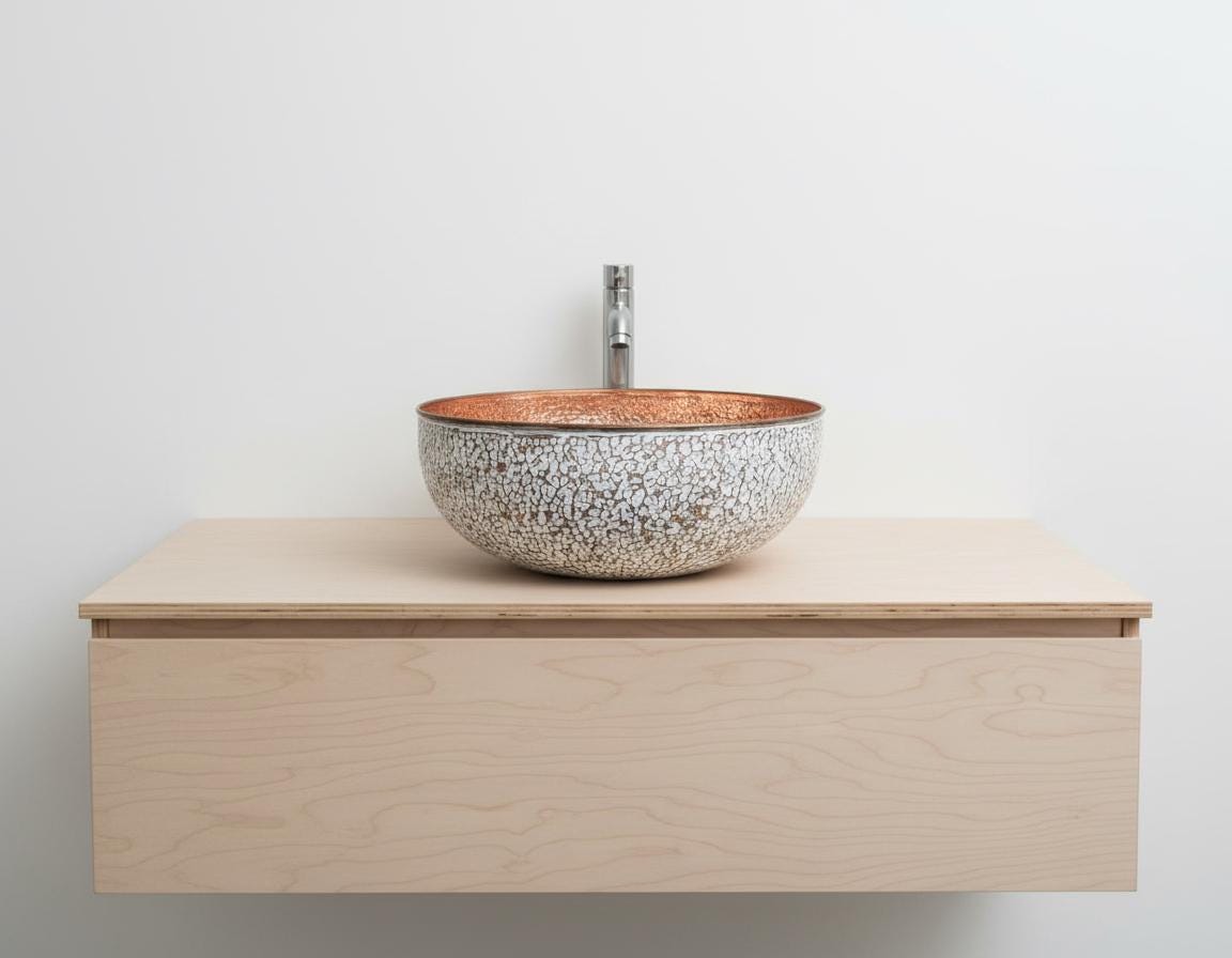 Bathroom vanity with a speckled ceramic sink on a light wood cabinet against a white wall.