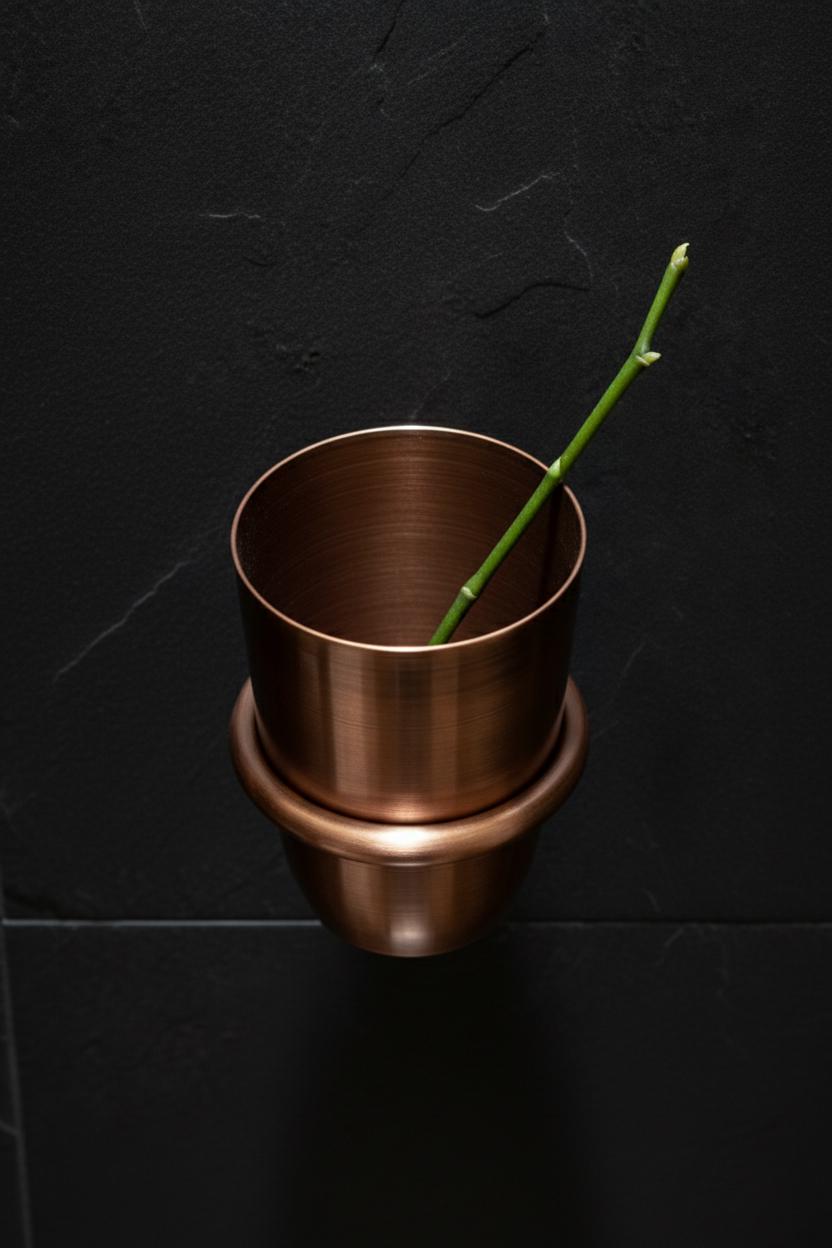 Bronze planter with a green plant stem against a black background