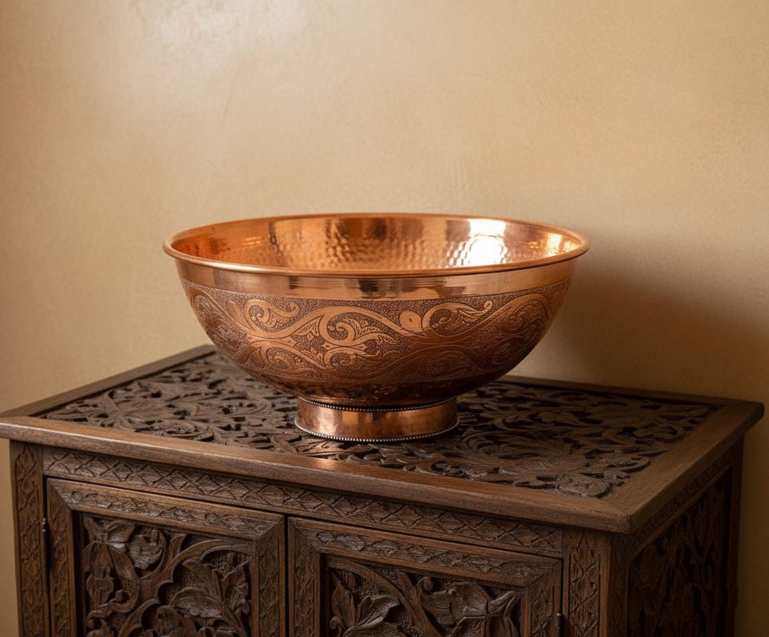 Copper bowl with intricate designs on a wooden cabinet against a beige wall