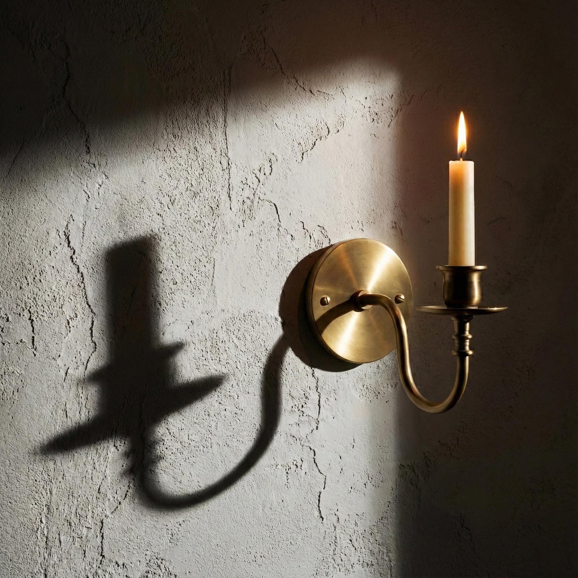 Brass wall sconce with a candle casting a shadow on a textured wall.