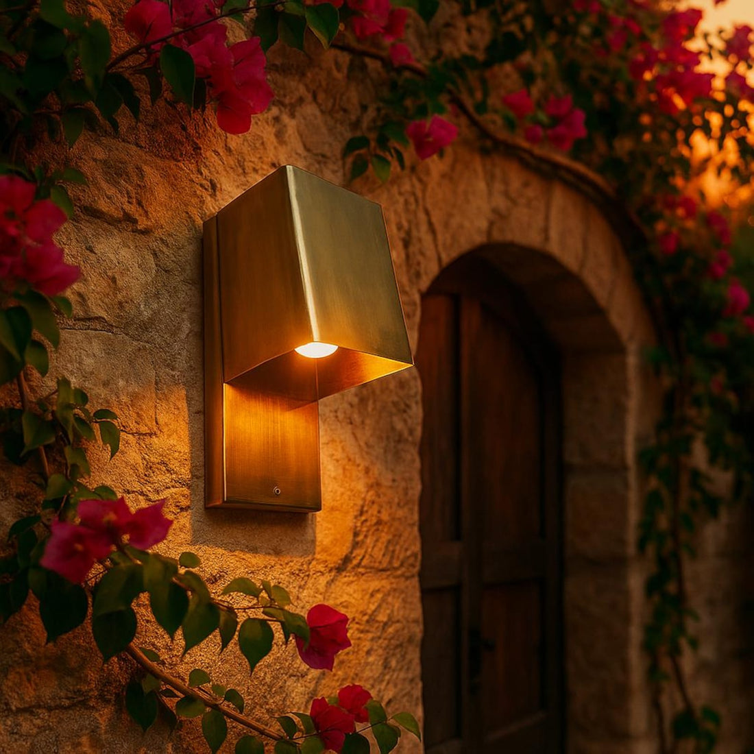 Gold outdoor wall light fixture on a stone wall with pink flowers
