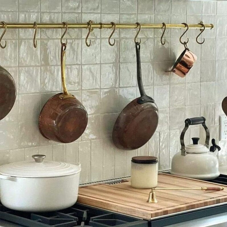 Wall-mounted solid brass pot rack holding copper pans and kitchen utensils

